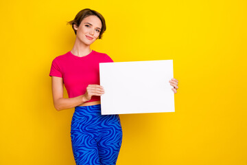 Fototapeta na wymiar Photo of pretty sweet woman dressed pink t-shirt holding white placard empty space isolated yellow color background