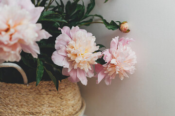 Naklejka na ściany i meble Beautiful peonies bouquet in basket in modern boho room. Gentle pink peony flowers on rustic background, moody image. Modern bohemian decor, stylish comfy interior details