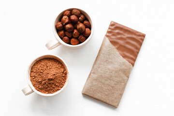Open chocolate bar with hazelnuts and cocoa in a bowl on a white background