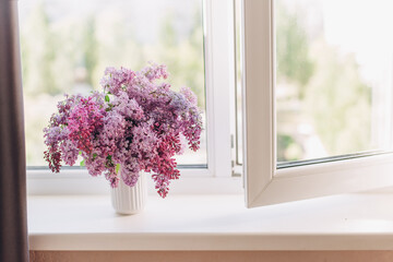 Vase with a bouquet of spring lilac flowers on the windowsill
