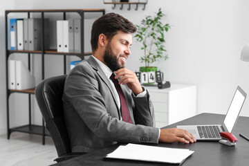 Handsome young businessman working with laptop at table in office