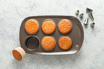 Tray with tasty muffins and piping tips on light background