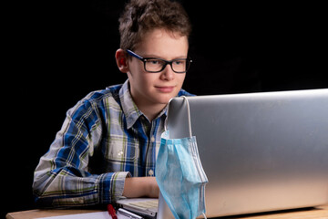 Boy with curls and glasses and checked shirt works intently on laptop. Mouth guard, mask and...