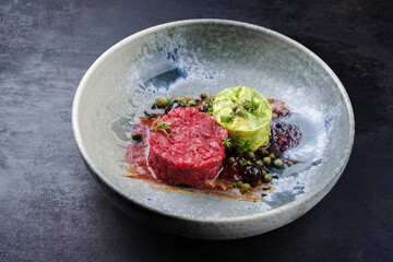 Modern style gourmet tartar raw from chianina beef filet with avocado and capers in amareno cherry and truffle sauce served as close-up on a Nordic design bowl