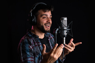 Hombre cantor grabando su voz con microfono de condensador y auriculares - obrazy, fototapety, plakaty