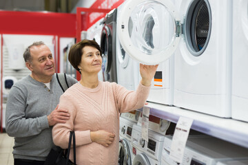 Happy spouses of mature age, who came to the electronics and household appliances store for shopping, choose a washing ..machine