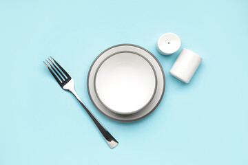 Clean dishware and fork on blue background