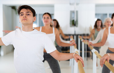 Fototapeta na wymiar Diligent young man engaging in ballet at ballet barre in training hall during workout session
