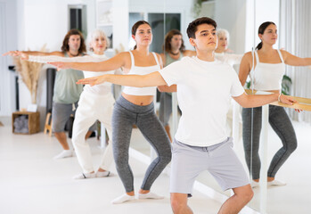 Fototapeta premium Diligent young man engaging in ballet at ballet barre in training hall during workout session