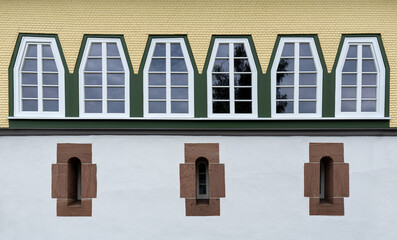 Reihe von trapezförmigen Fenstern über drei sehr schmalen Fenstern mit Steinrahmen in restaurierter Fassade