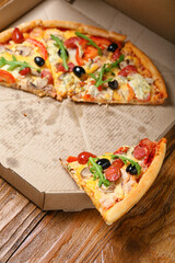 Cardboard box with pieces of tasty pizza on wooden background, closeup