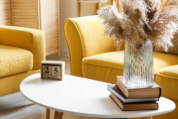 Cube calendar with date SEPTEMBER 25 and pampas grass in vase on table near yellow sofa