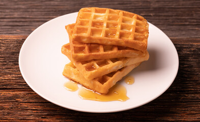 Delicious Belgian waffles with honey served on white plate and wooden background, rustic concept.