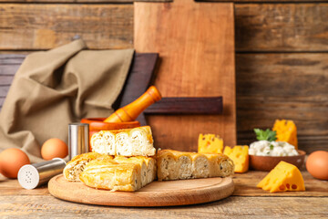 Board with pieces of delicious cheese pie and ingredients on wooden table