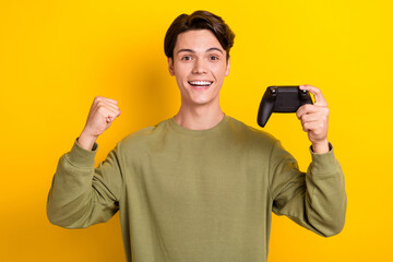 Photo of positive overjoyed man wear khaki stylish clothes raise hands fists yes hooray win competition isolated on yellow color background