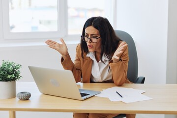 Business woman working in office at desk with laptop, anger and argument, discussing business processes online via video link, online director
