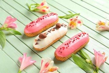 Obraz na płótnie Canvas Delicious eclairs and beautiful flowers on green wooden background