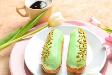 Plate with delicious eclairs and beautiful flowers on light background
