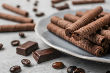 Plate of delicious rolled wafer cookies with coffee beans and chocolate pieces on grunge background, closeup
