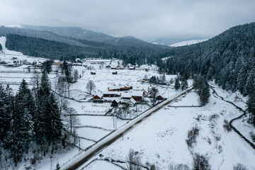 Aerial view of pine forest and a small village covered by snow in Carpathian Mountains of Romania, Rarau Mountains region. Cloudy weather conditions