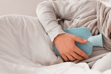 Ill man lying with hot water bottle in bedroom, closeup