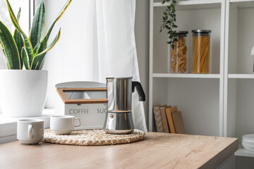 Fototapeta na wymiar Wicker coaster with geyser coffee maker on kitchen counter near window