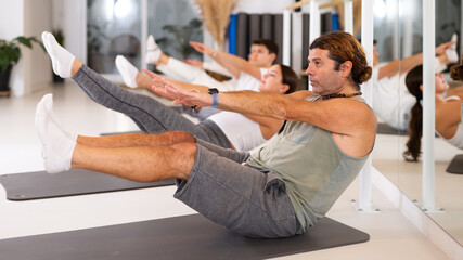 Diligent middle-aged man practicing pilates in training area during pilates classes