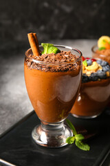 Board with glass of delicious chocolate pudding, cinnamon and mint on black and white table