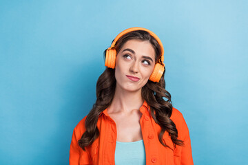 Photo of young attractive woman wear headphones look skeptical empty space dressed stylish orange look isolated on blue color background
