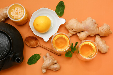 Composition with teapot, cups of tea, honey, mint, lemon and spoon on orange background, closeup