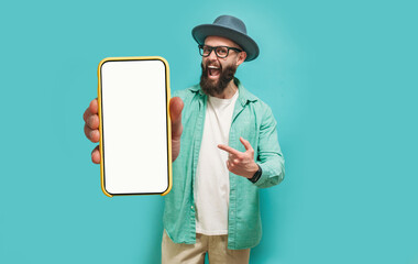 Young crazy bearded charismatic hipster showing big empty white smartphone screen for copy space and advertising area isolated on blue studio background. Mobile App Advertisement. Display Mock Up