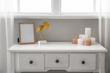 Burning candles and blank frame on table near window