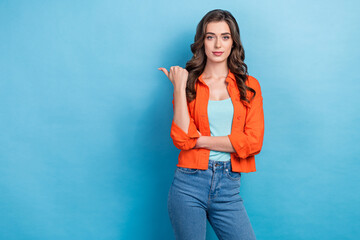 Fototapeta na wymiar Photo of adorable confident lady wear orange jacket pointing thumb empty space isolated blue color background