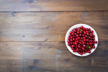 ripe red cherries in a white plate on a wooden background with copy space