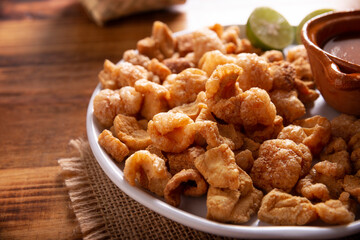 Chicharrones. Deep fried pork rinds, crispy pork skin pieces, traditional mexican ingredient or snack served with lemon juice and red hot chili sauce.