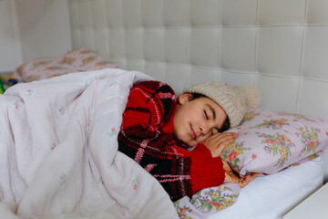 side view of girl wearing beige warm hat sleeping in the bed under blanket