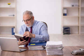 Old male boss reading book at workplace