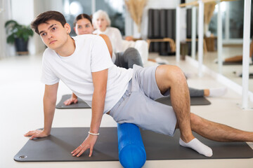 Fototapeta na wymiar Sporty slender males and females doing exercises with pilates roller during group training at gym. Healthy lifestyle concept.