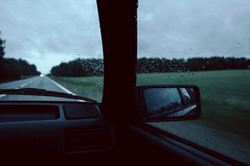 View though Audi 80 front windshield as driving on rainy summer evening with raindrops on glass