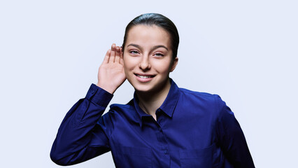 Young female holding hand near ear, listening attentively, on white background