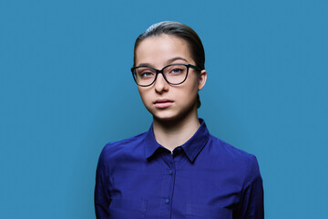 Headshot portrait of young female student looking at camera on blue background