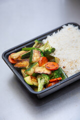 A view of a plastic to-go container filled with steamed white rice and wok-fried veggies.