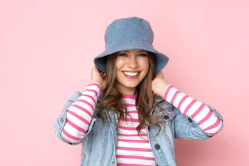Very positive young woman in denim outfit on pastel pink background.