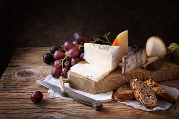 Assorted cheese: Pecorino rosso, Blu di bufala, Pecorino toscano, Formaggio al pepe. Cheese platter, with bread, grapes and pear on wooden table, space for text.