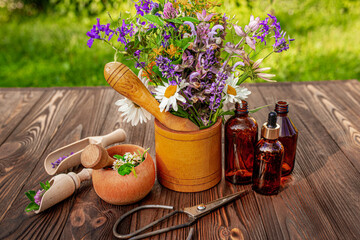 A wooden mortar with a selection of medicinal herbs on the table on a bright sunny day.