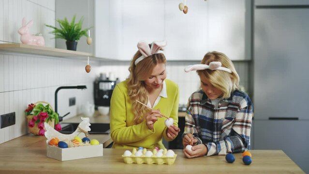 Happy mother and son in kitchen sitting, painting eggs for traditional spring dinner. A smiled family is preparing for easter. Easter, family, holiday and children concept