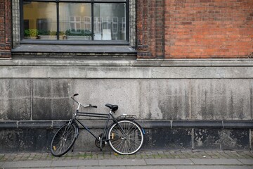 Black bicycle standing against an orange brick wall under a window along the Nyhavn Canal in Copenhagen, Denmark