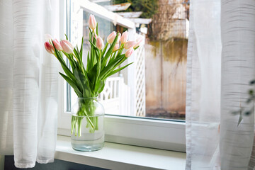 Bouquet of beautiful spring pink tulips in a vase on a windowsill on a sunny day