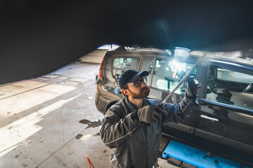 An expert mechanic with an LED light inspects a car on a lift in a repair station. High-quality photo