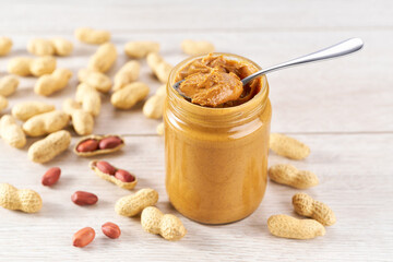 Glass jar with creamy peanut butter on  white wooden table.